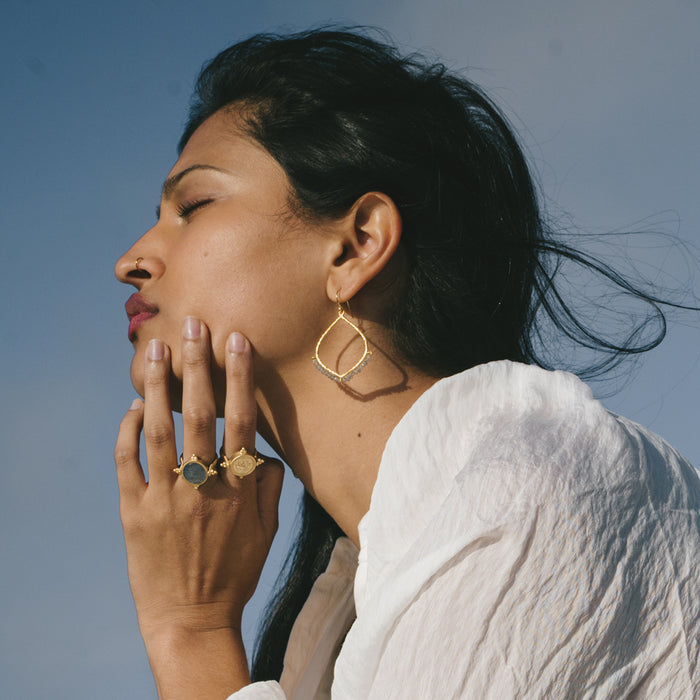 Gold-tone lotus petal-shaped earrings with dark labradorite stone centers, worn on model's ears.