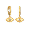 Gold huggie hoop earrings with evil eye charms featuring crystal centers and textured detailing.