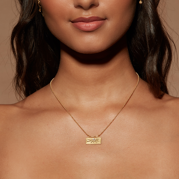 Model wearing the April White Topaz Sunburst Birthstone Tablet Necklace, showcasing its elegant gold design and sunburst engraving. This meaningful charm highlights the connection to zodiac energies, providing spiritual support and enhancing the meditation experience.