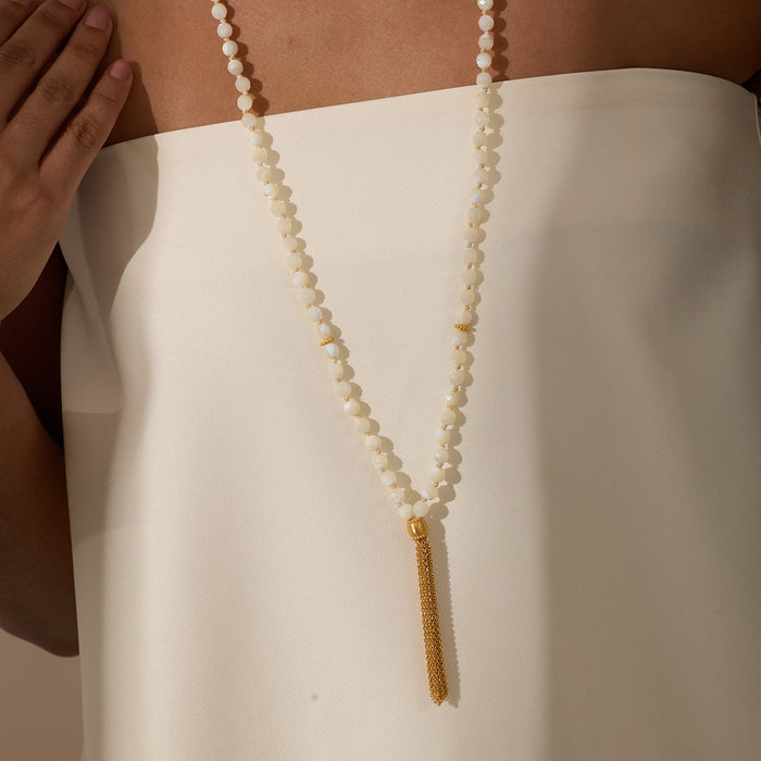 Beaded mala necklace with cream-colored round beads and gold tassel pendant worn over white garment.
