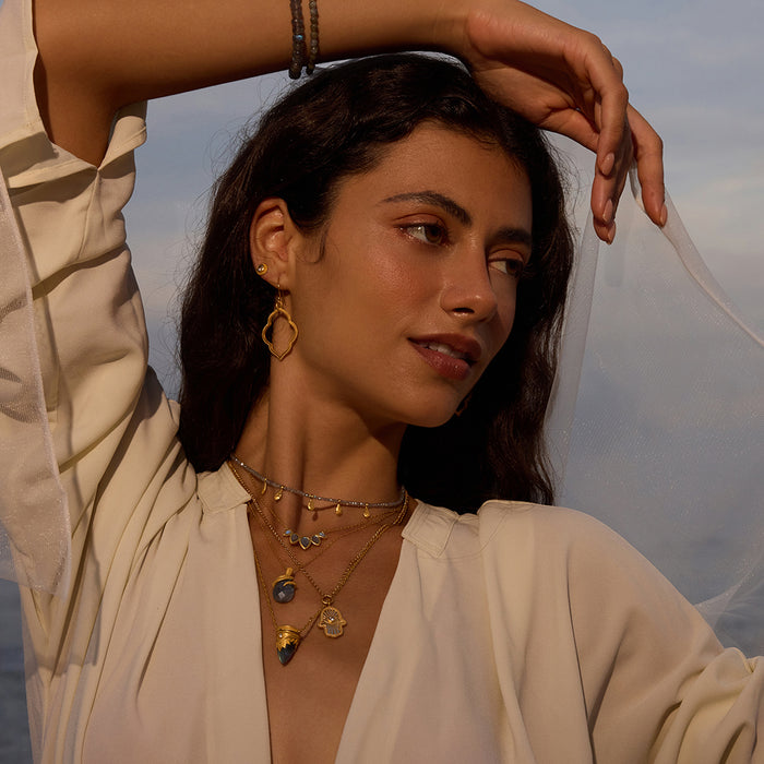 A beautiful woman showcasing multiple layers of spiritual jewelry, including the Inner Knowing Labradorite Snake Necklace, capturing a bohemian vibe. This meditative jewelry collection brings together elements of the sun, moon, and zodiac, symbolizing deep meaning and powerful manifestation.
