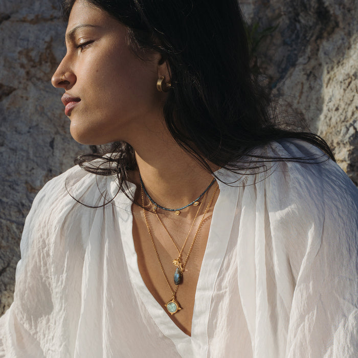 Woman wearing layered gold chain necklaces with blue-gray labradorite pendants and lotus charm on cord.