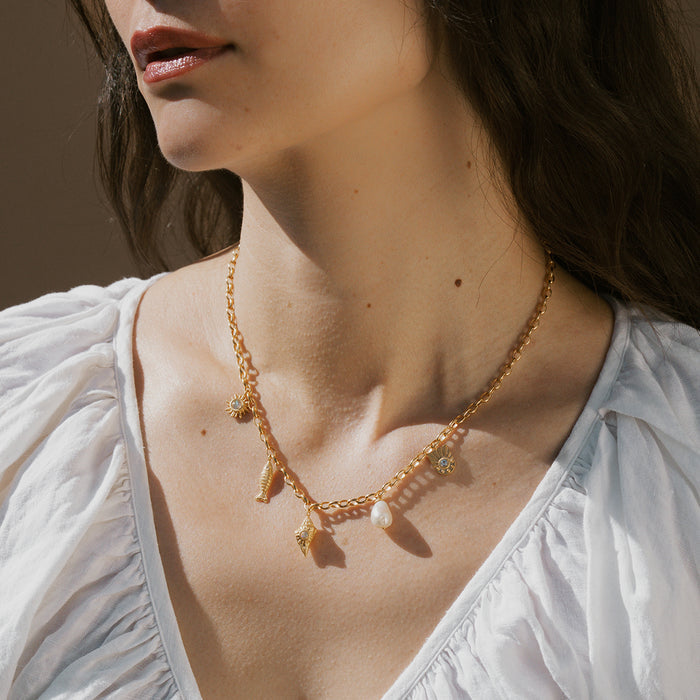 Gold-tone chain necklace with sea-themed charms including shells and starfish pendants worn on model.