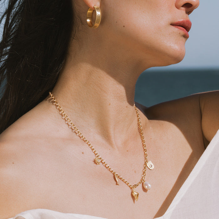 Gold chain necklace with shell, pearl, and crystal charms worn with matching gold hoop earrings.