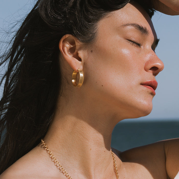 Gold hoop earrings with textured surface worn on model's ears in profile view.