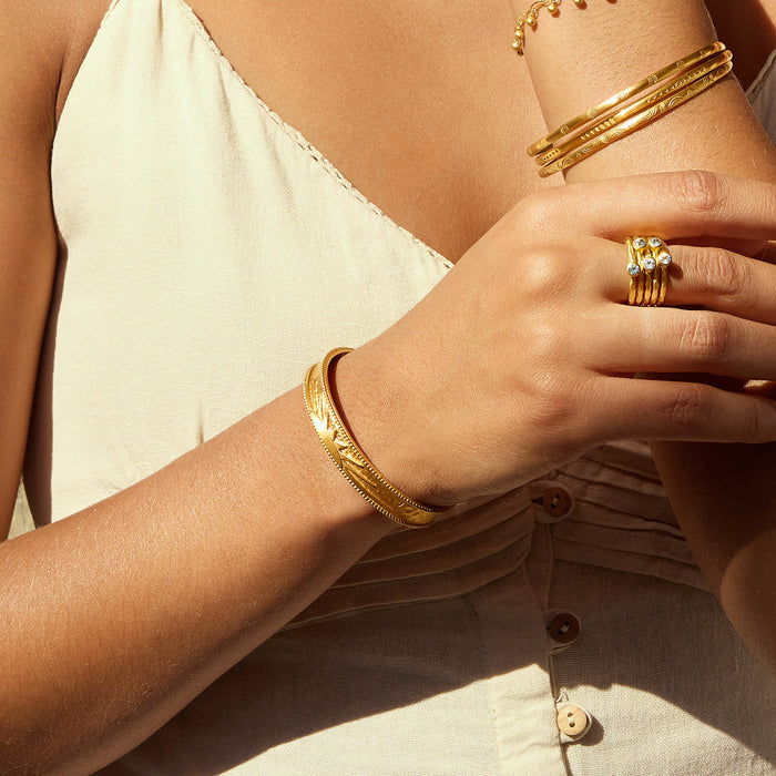 A person elegantly wearing the Breaking Dawn Sunrise Cuff bracelet along with multiple gold bracelets, ideal for those seeking spiritual jewelry. This chic combination symbolizes vitality and positivity, serving as a protective charm for meditation and daily intentions.