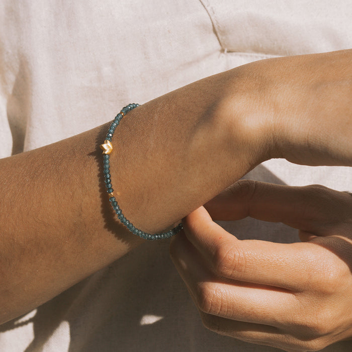 Blue topaz beaded bracelet with small gold lotus charm worn on wrist.