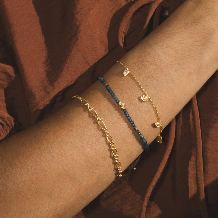 Three gold-toned bracelets stacked on a wrist, featuring dark blue beads and small lotus charm pendants.