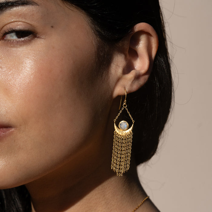 A close-up of a model wearing the Cascade of Starlight Moonstone Fringe Drop Earrings, highlighting the moonstone gem and graceful movement of the chains, reflecting the essence of spirituality, meditation, and zodiac energies in a meaningful talisman.