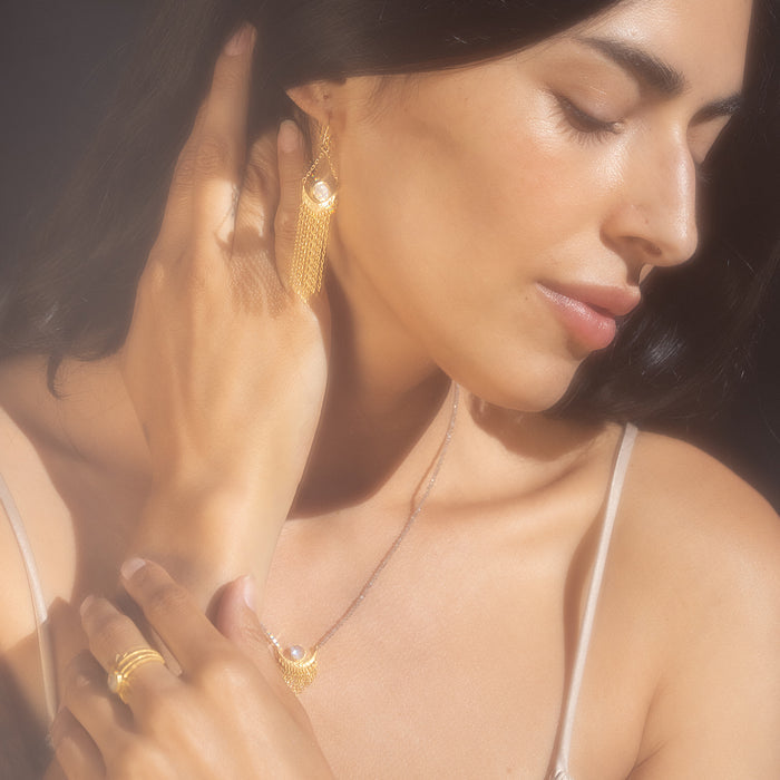 A woman showcasing the Cascade of Starlight Moonstone Fringe Drop Earrings, embodying spiritual jewelry and meditation. The delicate golden chains shimmer, representing a talisman for protection and meaning, perfect for manifestation in yoga practice.