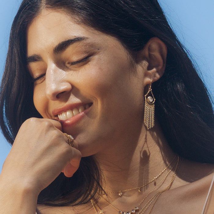 A joyful woman smiling while adorned with the Cascade of Starlight Moonstone Fringe Drop Earrings, embracing the essence of spiritual jewelry. These earrings serve as a talisman for hope and manifestation, ideal for yoga and meditation.