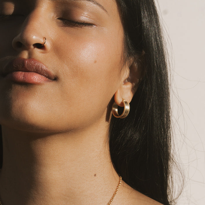 Gold-toned hoop earrings with textured finish worn on model's ear.
