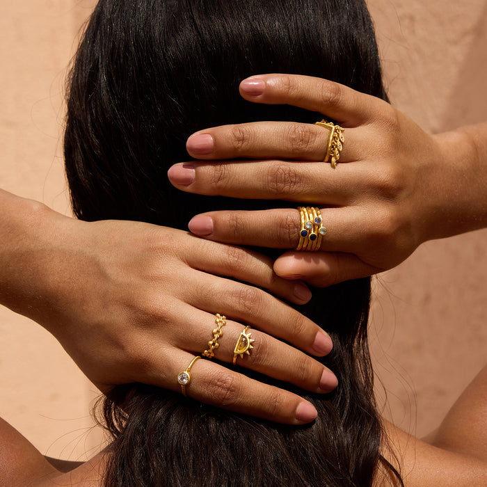 Gold petal ring with white topaz stone worn on hand with black hair background.