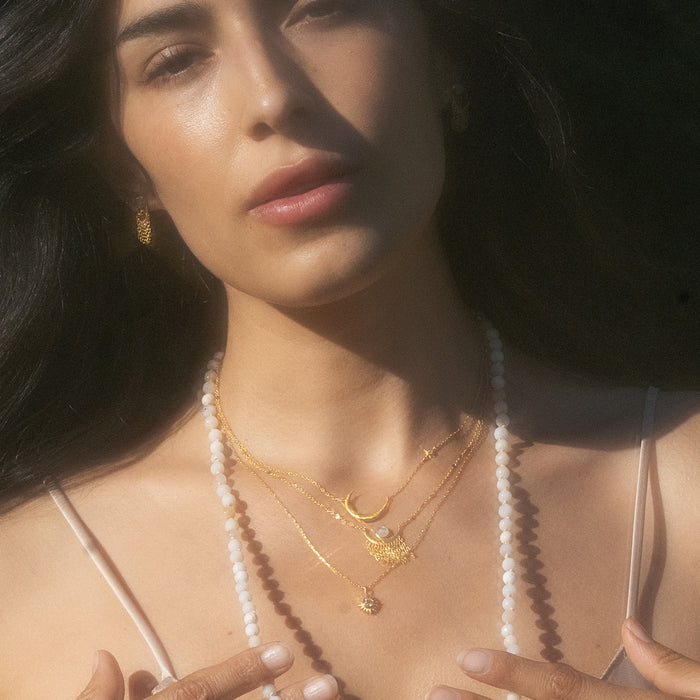 A woman showcasing layered necklaces including the Clarity White Topaz Starburst Necklace, embodying the essence of meaningful spiritual jewelry for meditation, protection, and inspirational talismans.