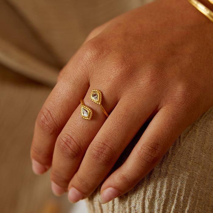 A close-up of the Commune with Love Blue Topaz Adjustable Ring worn on a hand, showcasing its delicate design with golden beads. This meaningful talisman enhances your spiritual journey and is ideal for yoga practitioners seeking a connection with the sun and moon.