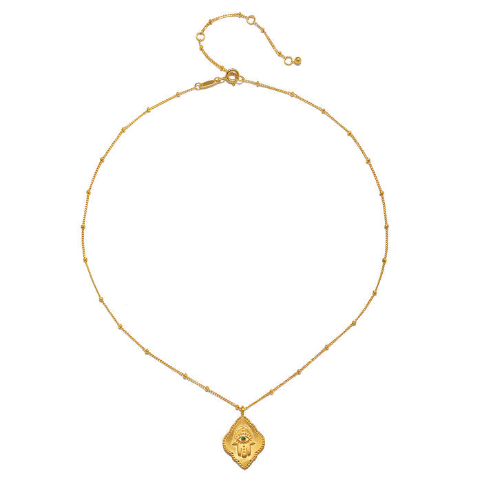 An elegant display of the Cradled in Protection Gold Hamsa Necklace on a plain background, emphasizing its craftsmanship and the themes of spirituality, protection, and yoga, making it a perfect talisman for manifestation and charm.