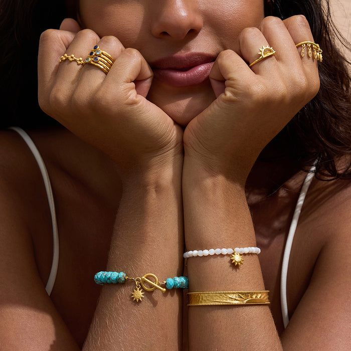 Stretch bracelet with white mother-of-pearl beads, gold-tone sun charm, and adjustable fit worn on wrist.