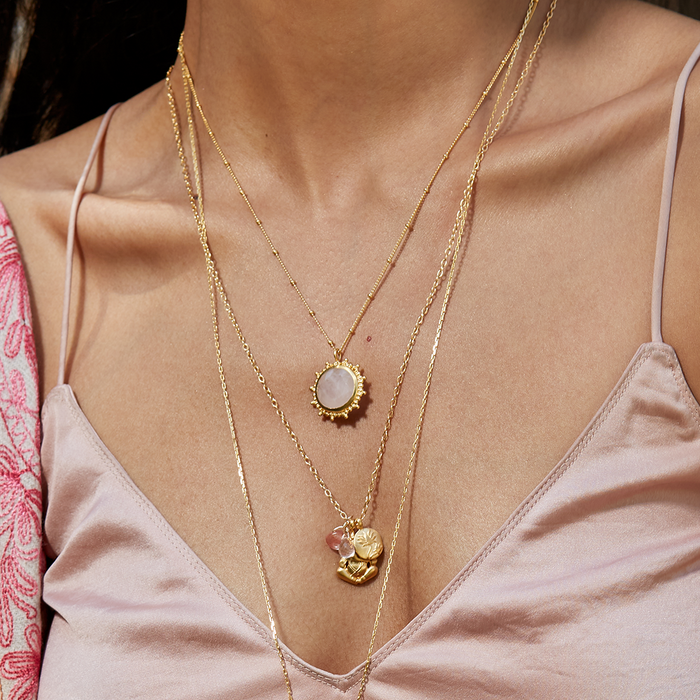 A model wearing the Drift Into Daydreams Moonstone Gemstone Necklace layered with other pieces, showcasing its elegant design perfect for yoga and representing spiritual and protective qualities.