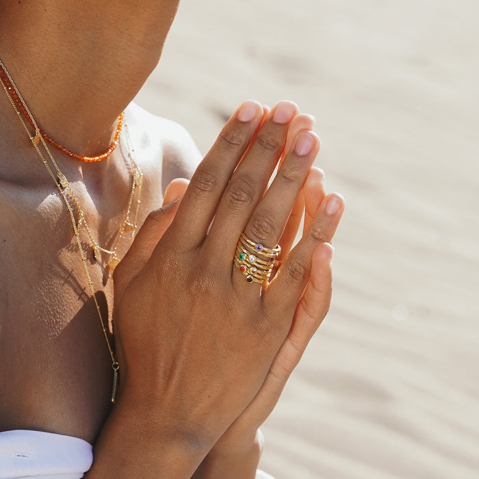Multiple stacked gold rings with colorful gemstones worn on hand.