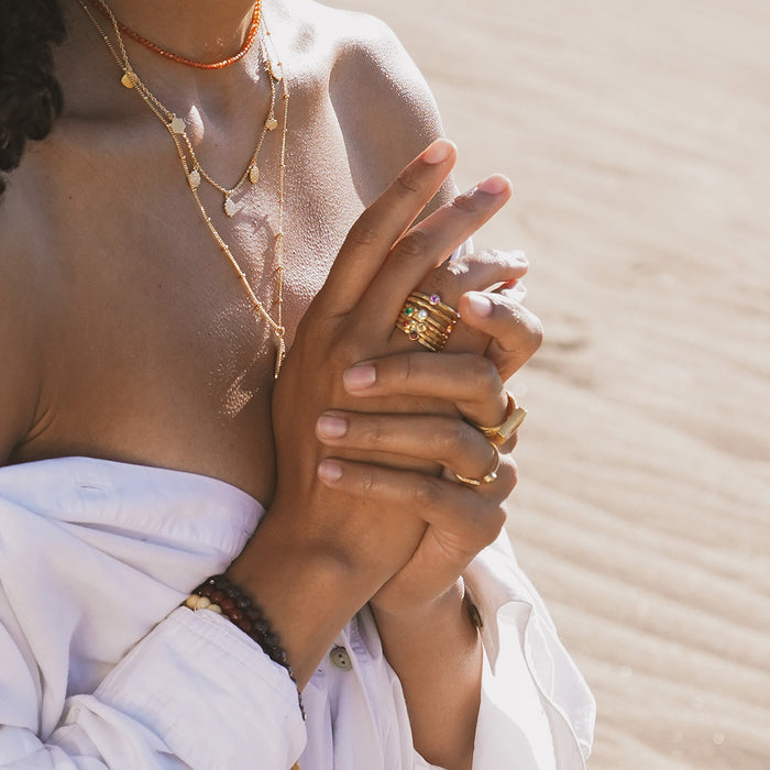 Gold-toned stacked rings with colorful gemstones worn on multiple fingers of a hand.