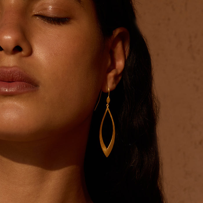 Gold-toned lotus petal drop earrings with elongated pointed oval shape worn on model with dark hair.