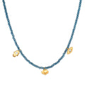 Blue faceted beads strung on a necklace with gold-toned charms including a lotus flower pendant and two eye-shaped charms.
