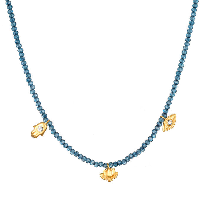 Blue faceted beads strung on a necklace with gold-toned charms including a lotus flower pendant and two eye-shaped charms.