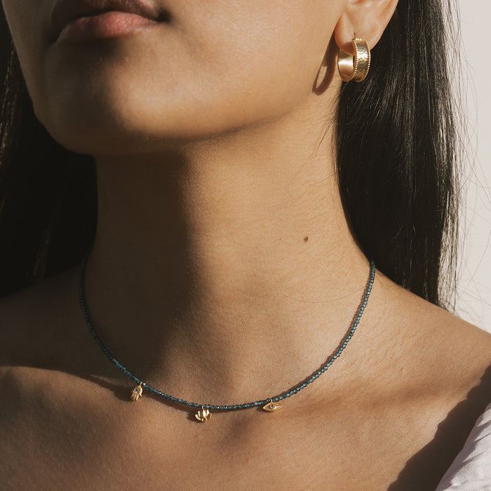 Blue beaded necklace with small gold charm pendants worn close to the neck.
