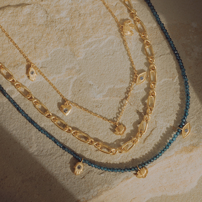 Layered gold-toned necklaces with blue topaz charms and a blue beaded strand on textured surface.