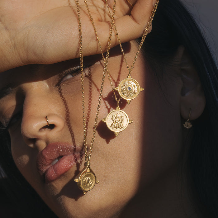 Gold-toned chain necklaces with circular coin pendants featuring embossed deity figures, worn layered on person.