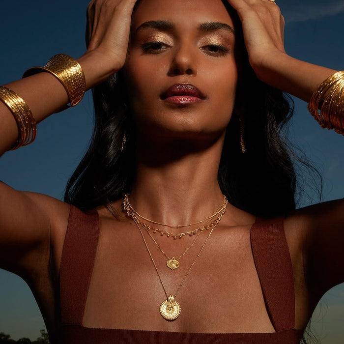 A striking image of a model wearing multiple layers of the Gold Mandala Necklace against a natural backdrop, blending the necklace's protective qualities with a serene vibe, suitable for mantra meditation and sacred practices.