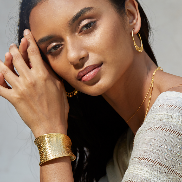 A close-up of a model wearing the Gold Medium Basketweave Bracelet Cuff alongside gold earrings and layered necklaces, emphasizing the bracelet's sacred aesthetic that resonates with yoga and meditation gifts.
