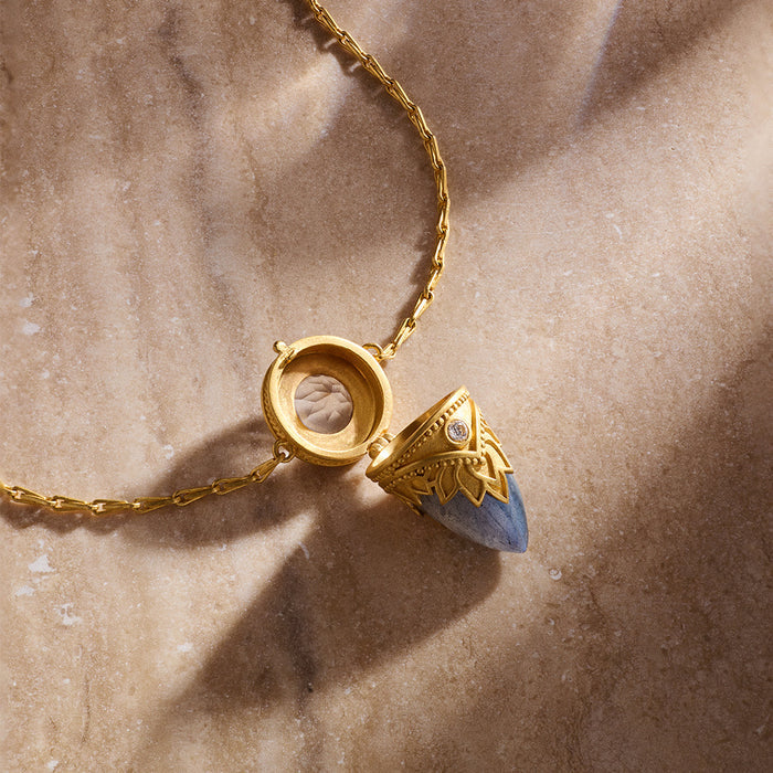 The Guiding Spirit Labradorite and White Topaz Lotus Locket Necklace resting on a smooth surface, representing spiritual jewelry that inspires transformation and supports the journey of manifestation and meditation.