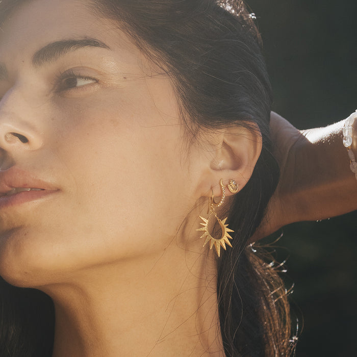 A profile view of a woman with Guiding Star Celestial White Topaz Stud Earrings, highlighting the harmonious blend of sun and moon motifs, embodying the essence of spiritual protection, meaningful meditation, and manifestation.