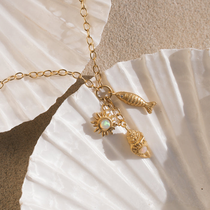 Gold chain necklace with sun charm, fish charm, and shell charm featuring opalescent stones.