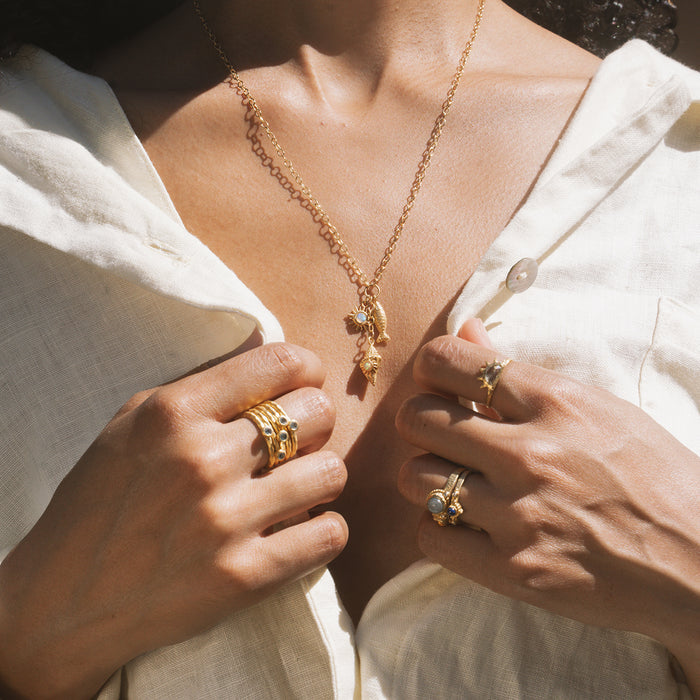 Gold chain necklace with leaf-shaped pendant and small charm worn on person in white shirt.