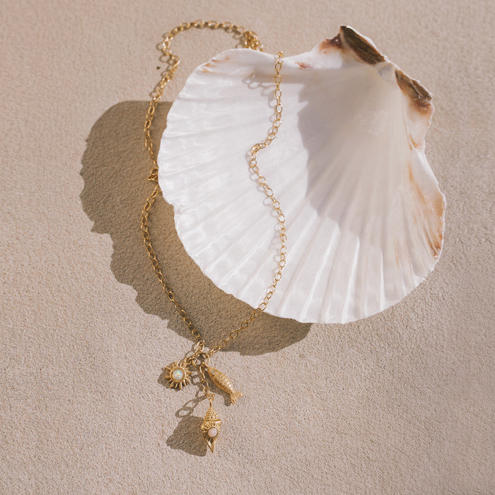 Gold chain necklace with white shell pendant and small gold charms including a sun motif and shell designs.