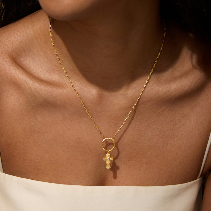 A close-up of the Honor Your Faith Cross Charm pendant, featuring an 18kt gold plated cross with a brilliant white topaz. This piece exemplifies spiritual jewelry, serving as a meaningful talisman for meditation and manifestation, perfect for yoga practices, while invoking protection and connection to the sun and moon.