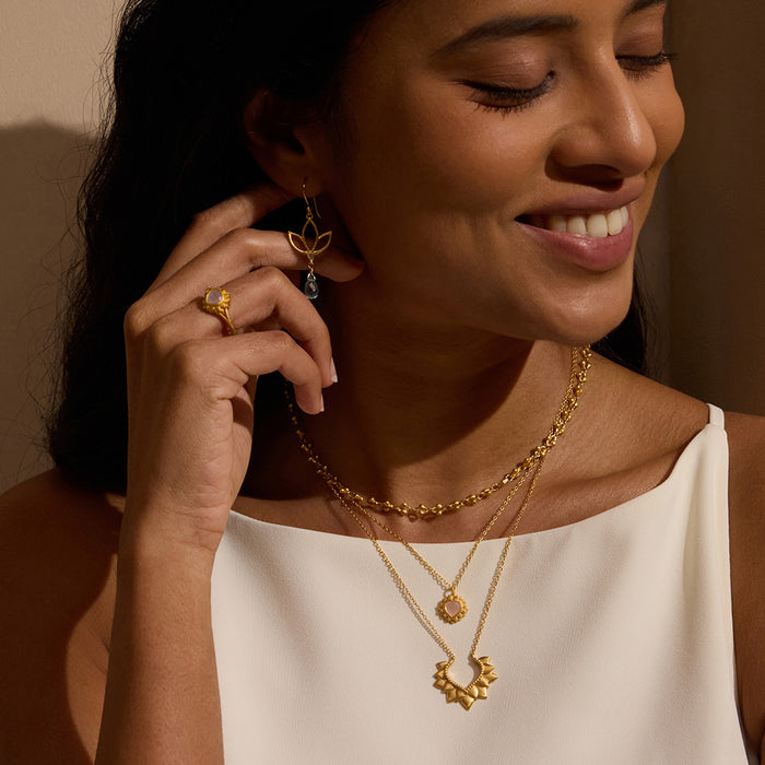 A joyful model wearing Ignite Renewal Blue Topaz Lotus Drop Earrings along with layered gold necklaces, showcasing spiritual jewelry perfect for yoga, meditation, and embodying the essence of protection and meaningful connections.