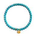 Turquoise beaded stretch bracelet with faceted round stones and a small gold-tone sun charm pendant.