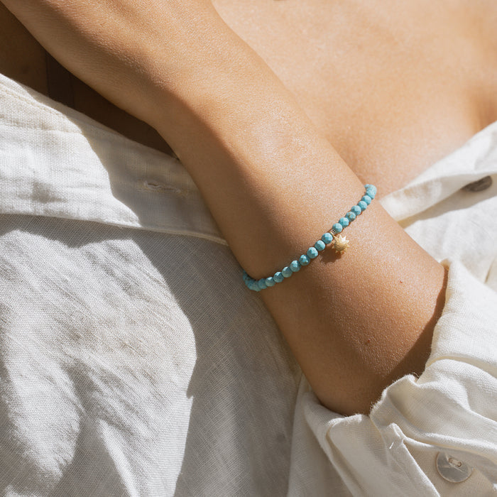 Turquoise beaded stretch bracelet worn on wrist with small gold charm detail.