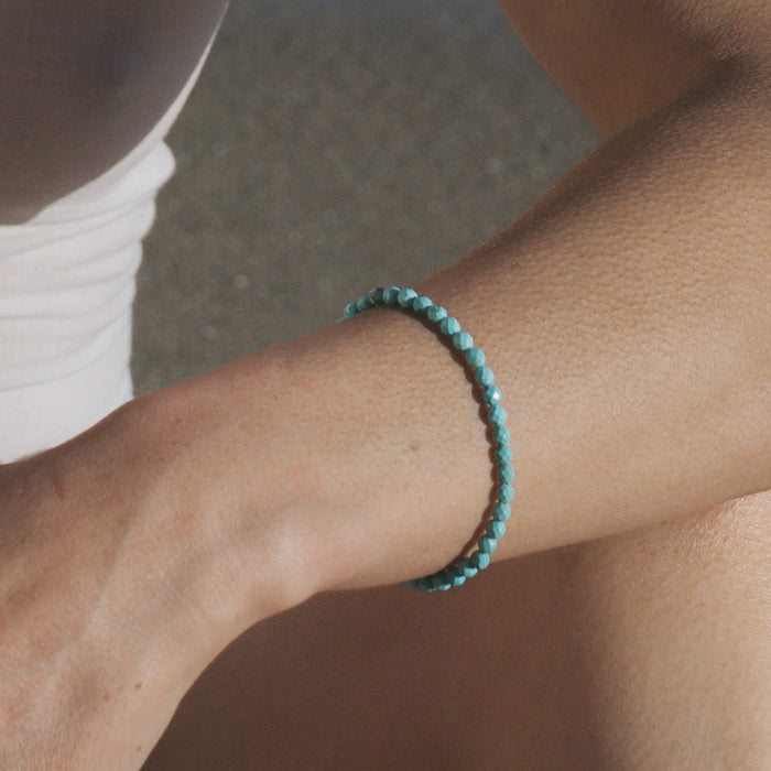 Turquoise beaded stretch bracelet worn on wrist with small round beads throughout.