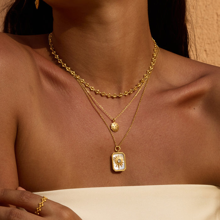 Gold-toned layered necklaces with textured chain, small round pendant, and rectangular sun pendant on white background.