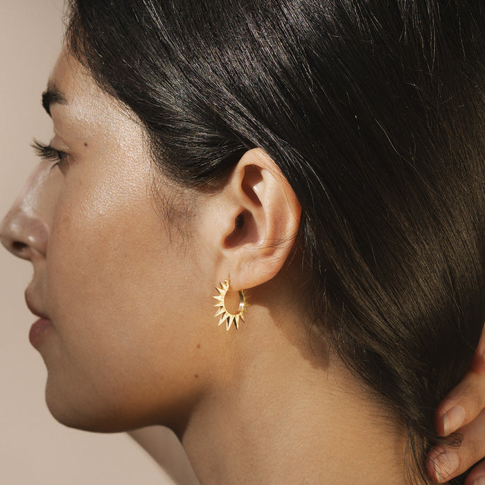 A woman wearing Incandescent Glow Starburst Hoop Earrings showcases their stylish design. These spiritual jewelry pieces symbolize guidance and inspiration, perfect for meditation and manifestation. Their sunburst motif represents meaning and protection, ideal for those who practice yoga or follow zodiac traditions.