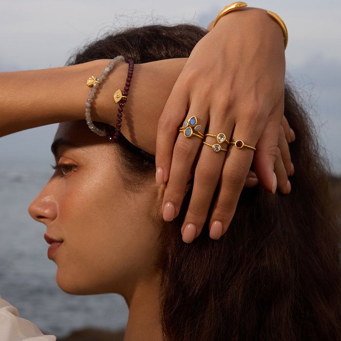 A serene image of a woman wearing the Second Sight White Topaz Ring along with other rings on a beach, embodying the spirituality of manifestation and connection to sun and moon energies.
