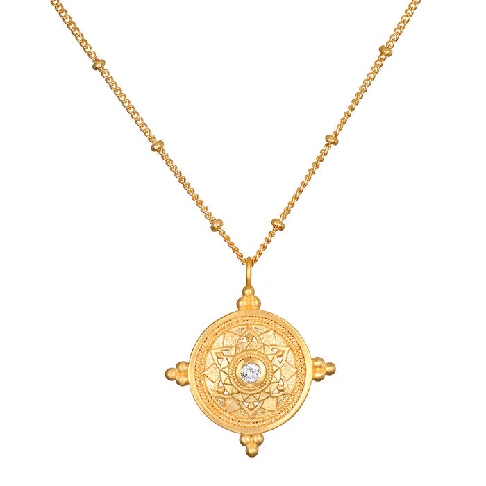 Gold chain necklace with circular mandala pendant featuring white topaz center stone and four decorative gold terminals.