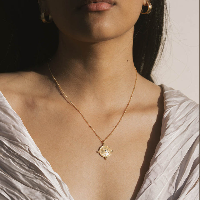 Gold chain necklace with circular mandala pendant featuring white topaz center stone, worn on model.