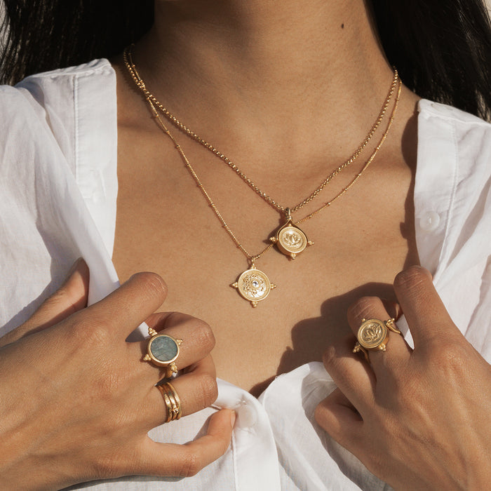 Gold-toned necklace with two circular mandala coin pendants featuring white gemstones, worn on person.