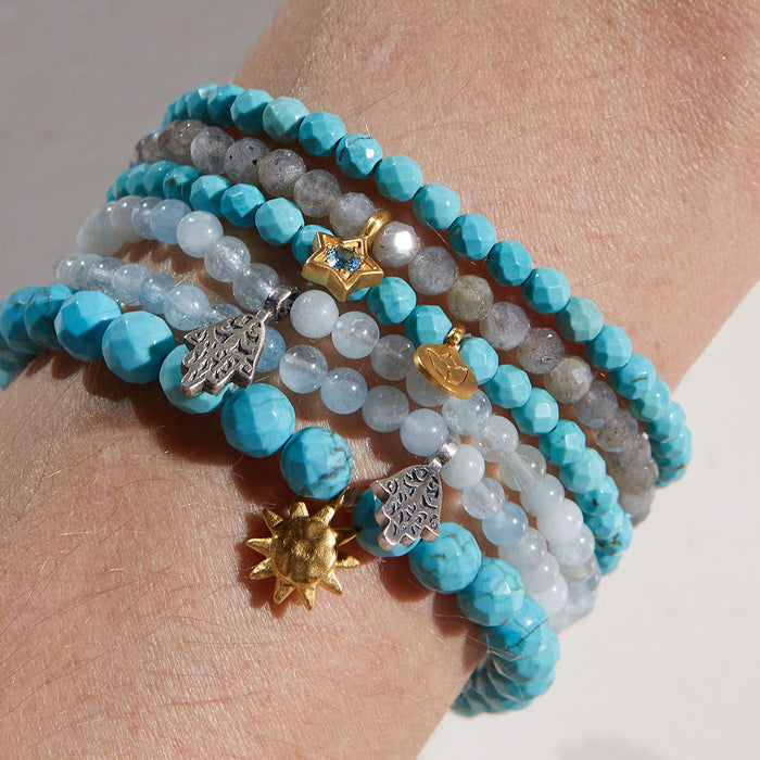 A stack of gemstone bracelets including the Inner Voice Lotus Gemstone Bracelet, showcasing vibrant turquoise and various charms. Ideal for yoga and spiritual practice, these malas serve as talismans for protection and meaningful self-expression.