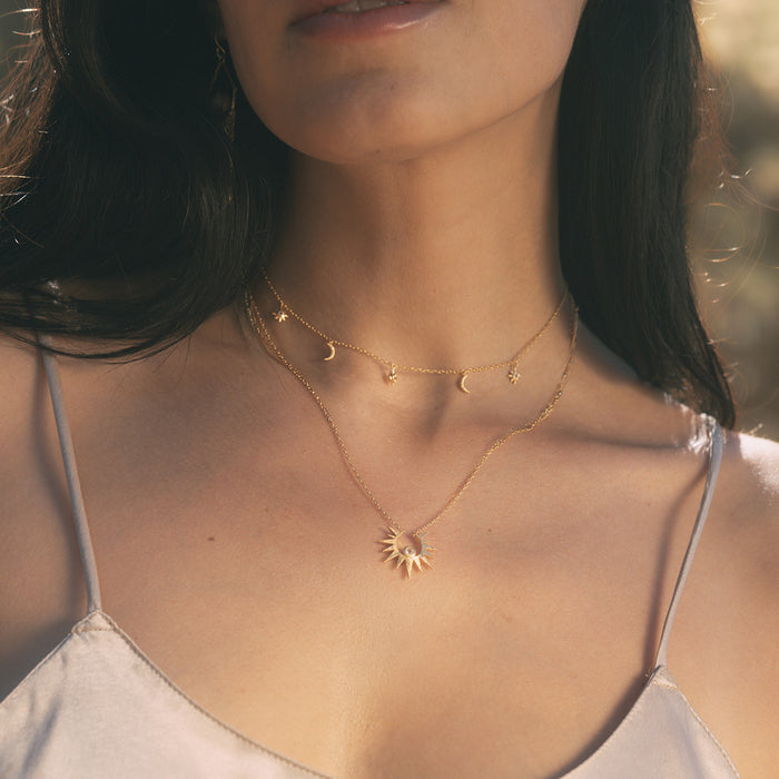 Two-piece gold necklace set with sun pendant and moon-and-star charm chain worn on model.